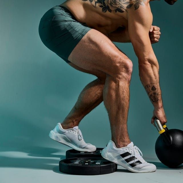 Tatuerad atlet gör en djup knäböj med kettlebell och viktskiva